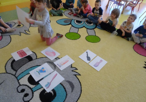 Dziewczynka unosi ilustrację przedstawiającą lusterko, w tle siedzą dzieci.